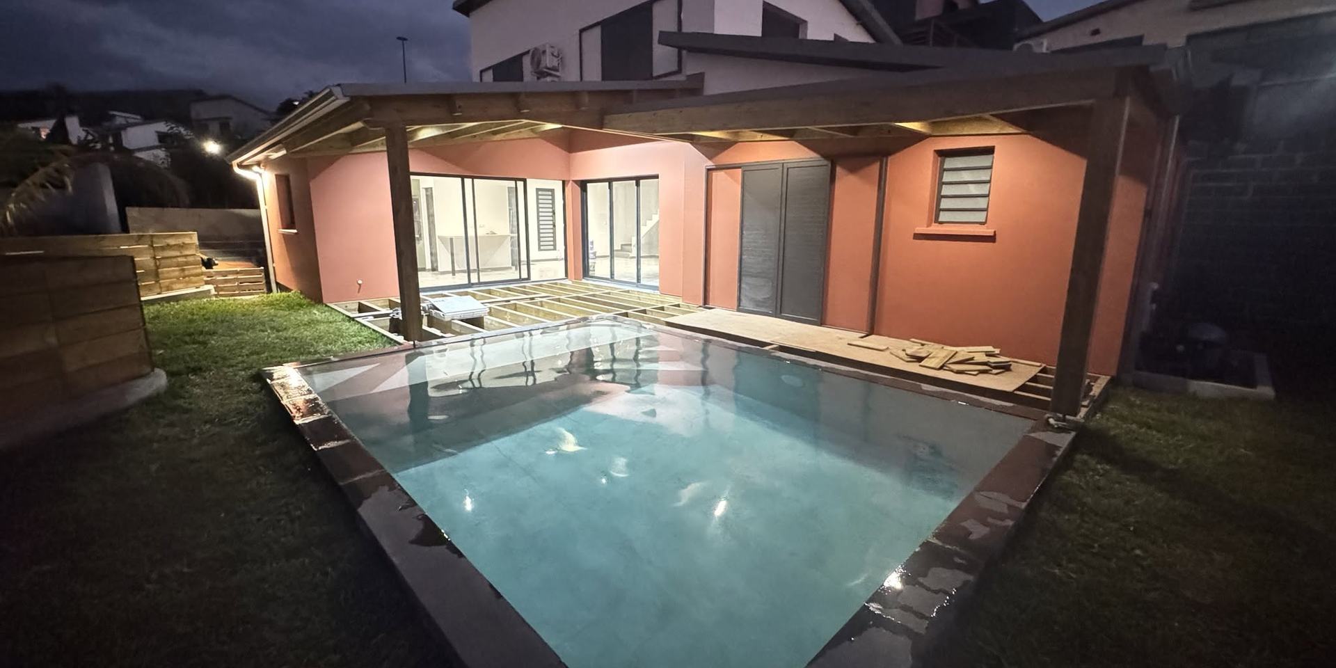 Maison individuelle avec piscine et varangue bois, éclairée à la tombée de la nuit