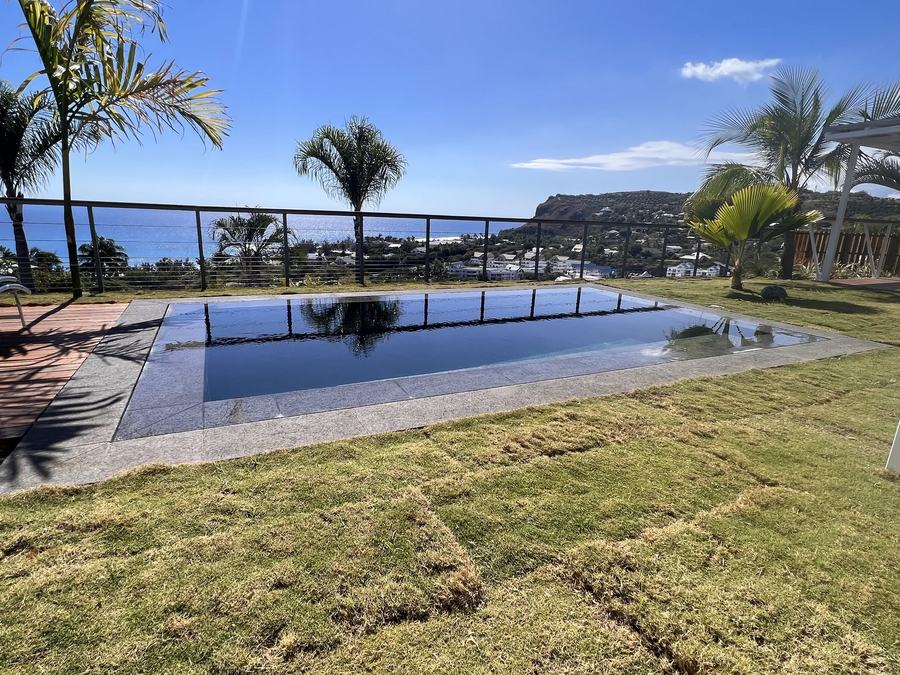 Piscine maçonnée avec plage en granit, pelouse et vue sur la mer